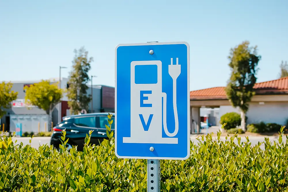 View of a city sign that has a symbol that stands for electric vehicle parking and charging. The sign has the letters "EV" written on it.