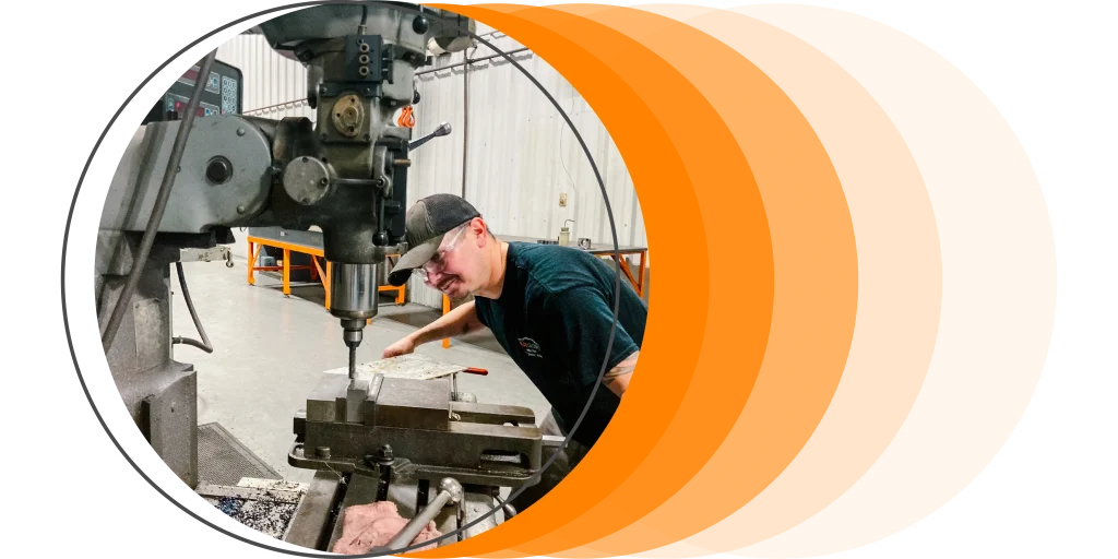 A person operates a large industrial milling machine in a workshop that has metal shaving on the machine's surface.